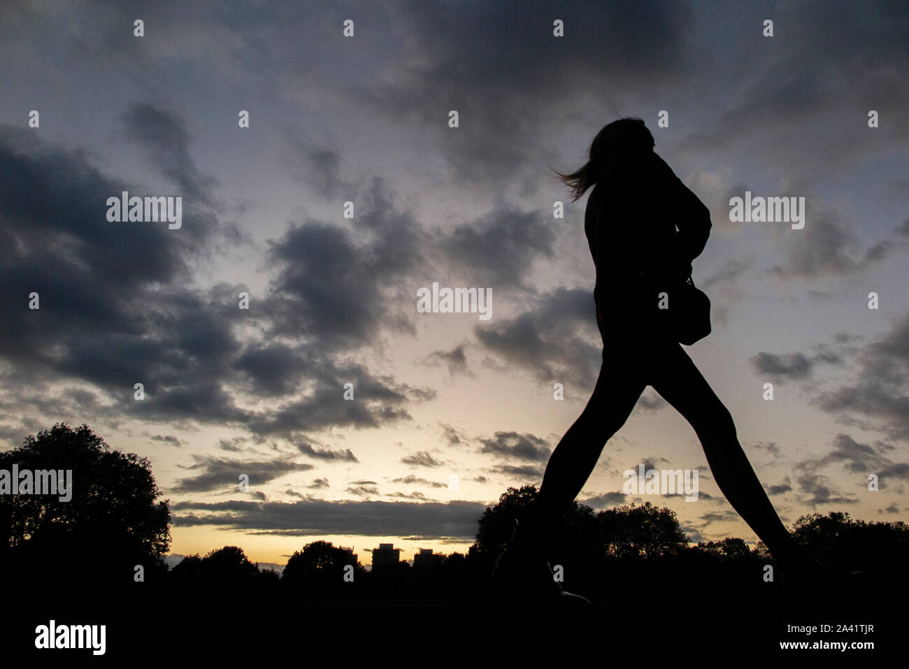 Una singola ragazza cammina home sotto un tempestoso tramonto in un parco di Londra Foto Stock