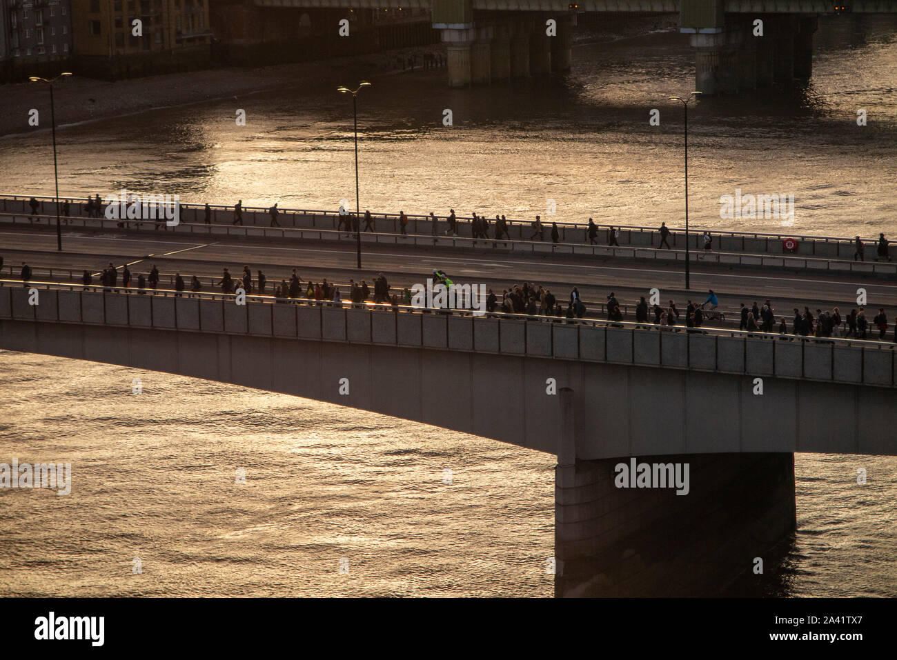 Fine della giornata lavorativa e pendolari a piedi oltre il Ponte di Londra come il sole tramonta Foto Stock