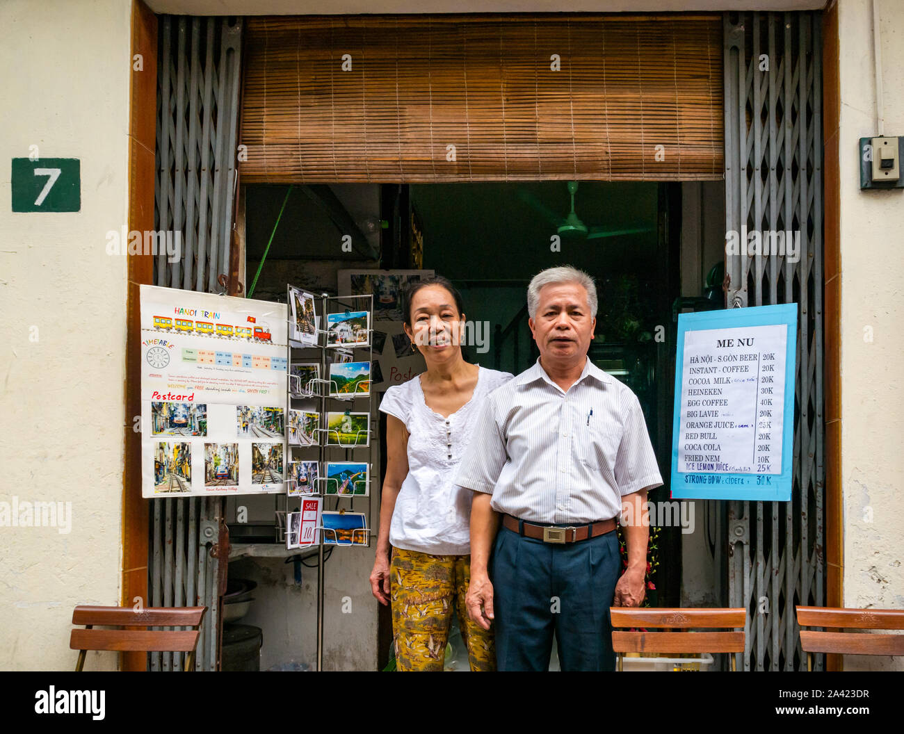 Coppia senior al di fuori della loro casa e caffetteria accanto alla linea ferroviaria, Villaggio Ferroviario, Hanoi, Vietnam Asia Foto Stock