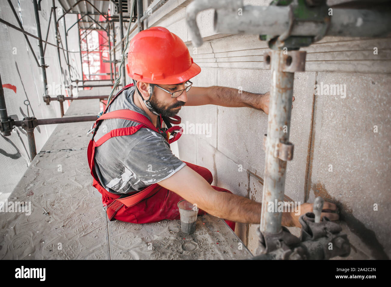 Costruzione mason lavoratore sul ponteggio la miscelazione di cemento e sabbia con la spatola sul sito di costruzione Foto Stock