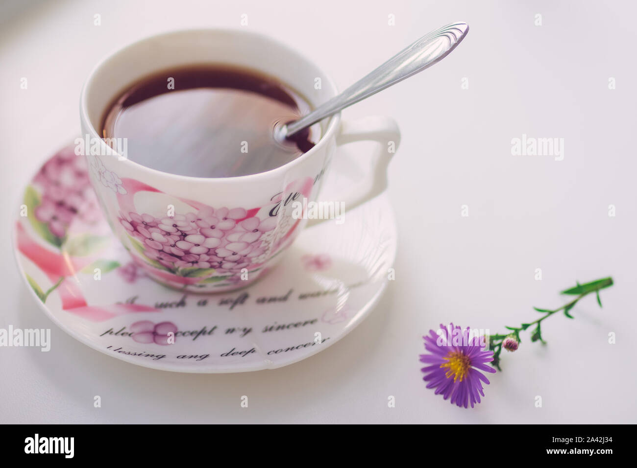 Tè nero con cucchiaio in un elegante vintage tazza di porcellana sul tavolo bianco. Fiore di gara crisantemo vicino a. Foto Stock