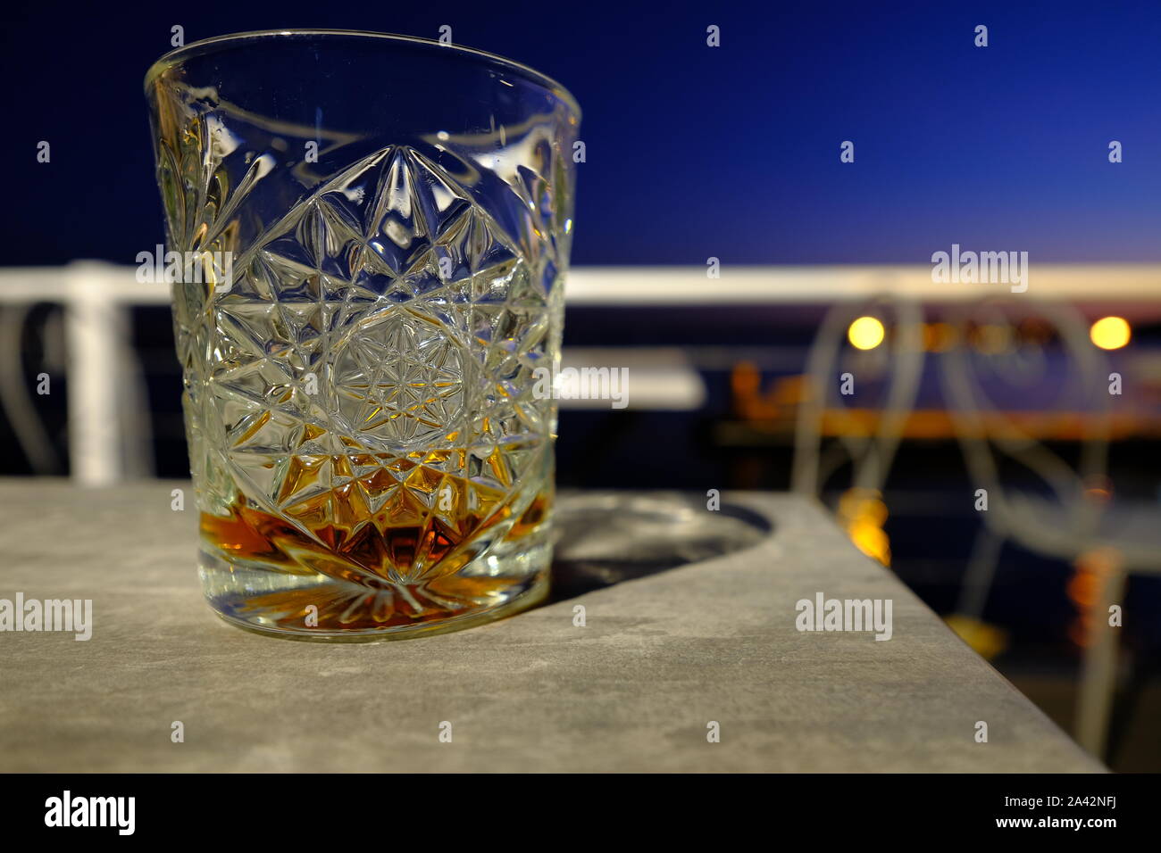 Whisky in vetro illuminato sulla sfocatura dello sfondo al tramonto Foto Stock
