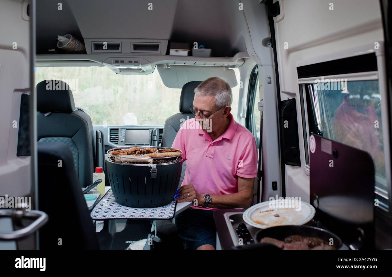 L'uomo negli anni settanta la cottura all'interno di un camper van mentre campeggio con la famiglia Foto Stock