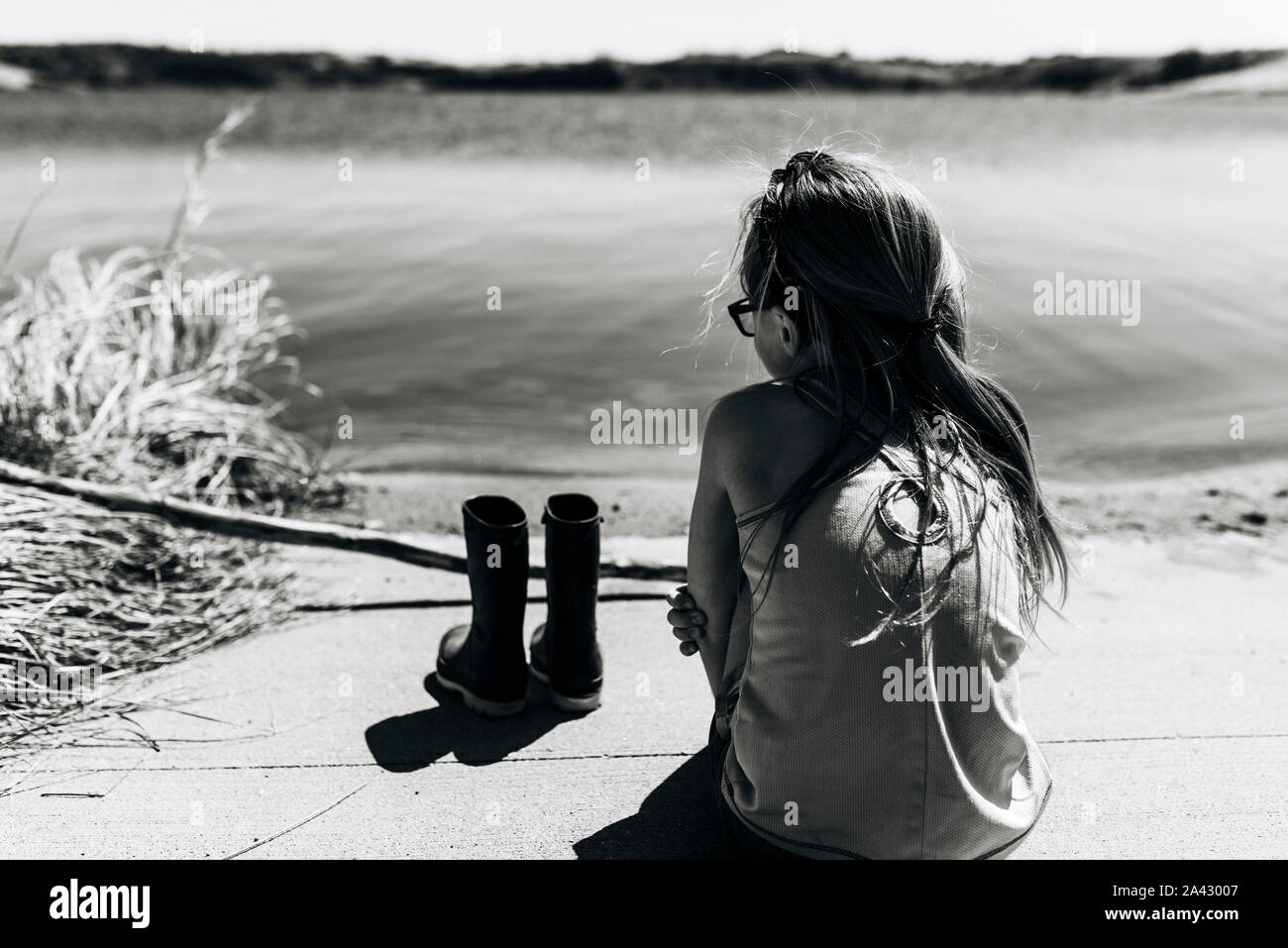 Bambina si siede accanto a lago con scarponi rimosso Foto Stock