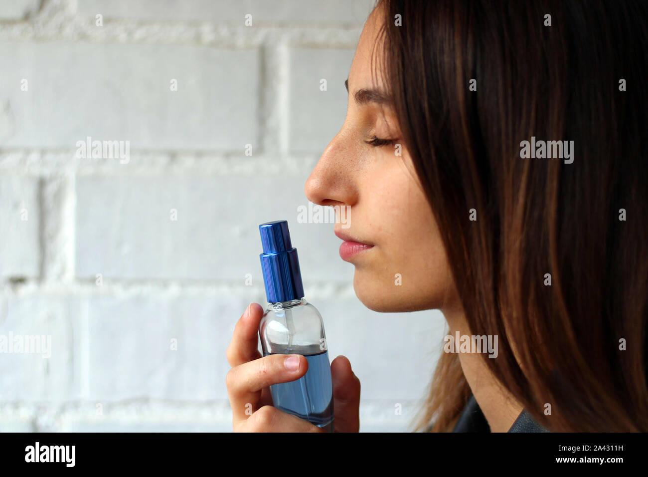Ragazza giovane e carina odorare un blu bottiglia di profumo. Buon profumo concetto. Foto Stock