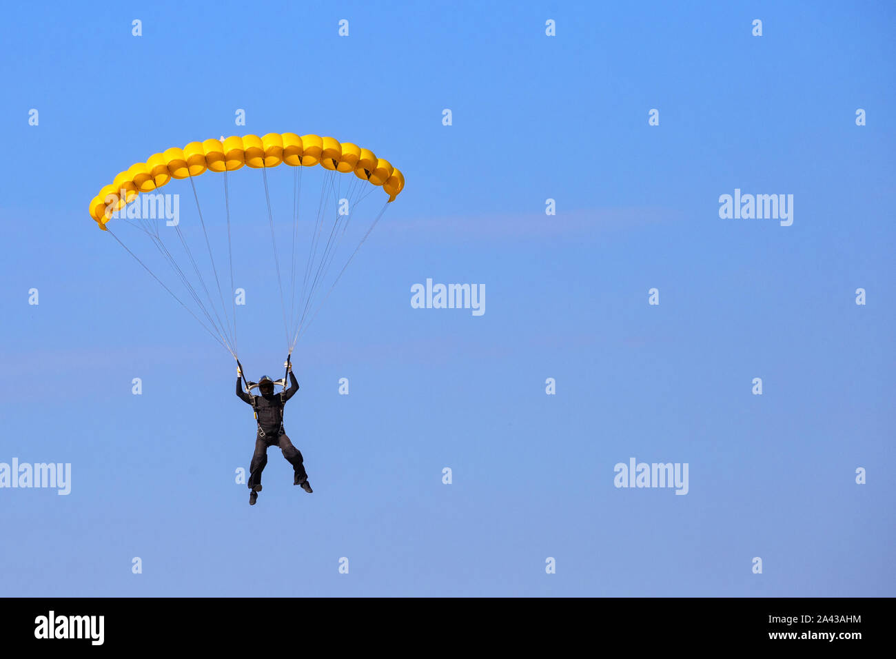 Paracadutista con un paracadute gialli nel cielo blu. I marchi e i loghi rimosso. La faccia nascosta dietro una maschera casco Foto Stock
