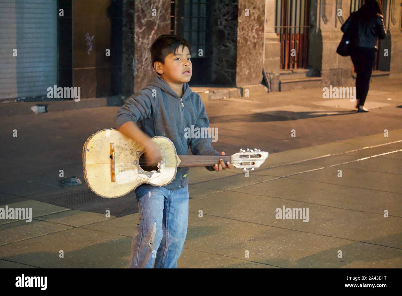 Ragazzo a suonare la chitarra su strada per i soldi con i pedoni dietro di lui su Ave 5 de Mayo, Centro Historico, Città del Messico, Messico Foto Stock