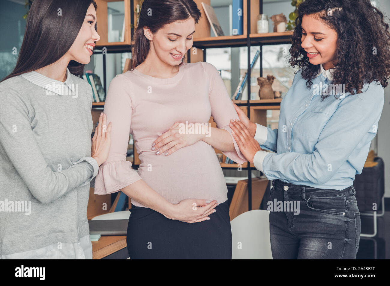 Startupers femmina lavorando insieme a Office in piedi che guarda alla pancia del collega incinta allegro Foto Stock