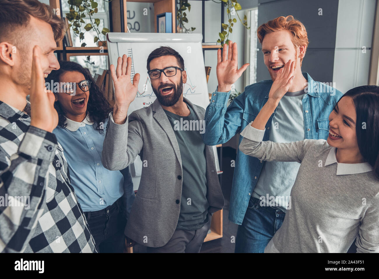 Startupers lavorando in ufficio insieme in piedi dando alta cinque allegro Foto Stock