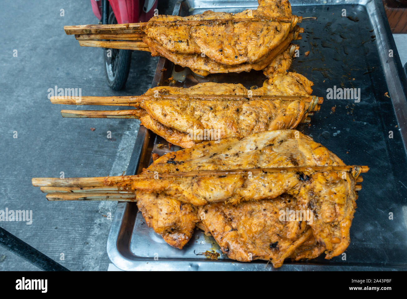 Chon Buri, Tailandia - 16 Marzo 2019: Nong mercato mon. Primo piano della appiattita pezzi di arrosto di carne di pollo su bastoni di legno in tre pali su metallo p Foto Stock