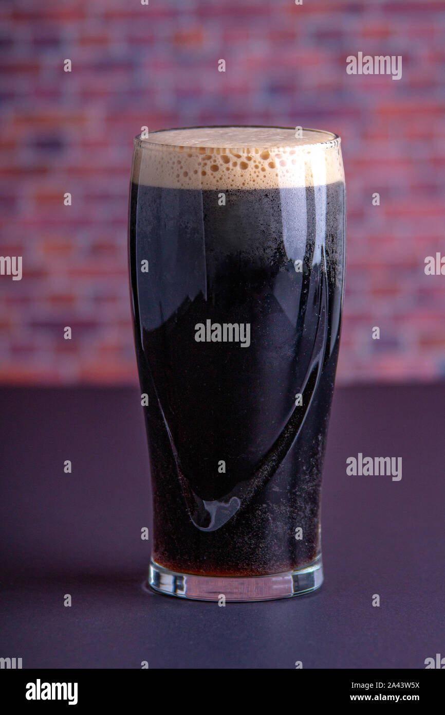 Una scura Guinness Irish Stout secca bicchiere di birra che ha origine nella fabbrica di birra a Dublino vista verticale Foto Stock