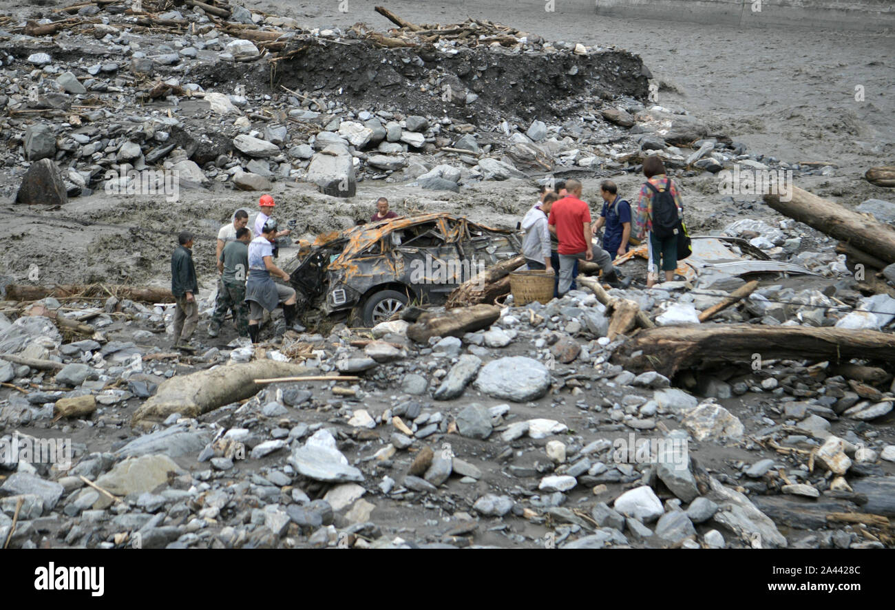 Loca residenti evacuare un auto danneggiata dopo essere stato colpito da più colate di fango attivato da pioggia pesante nel villaggio di Longtan, contea di Wenchuan, Aba Tibet Foto Stock