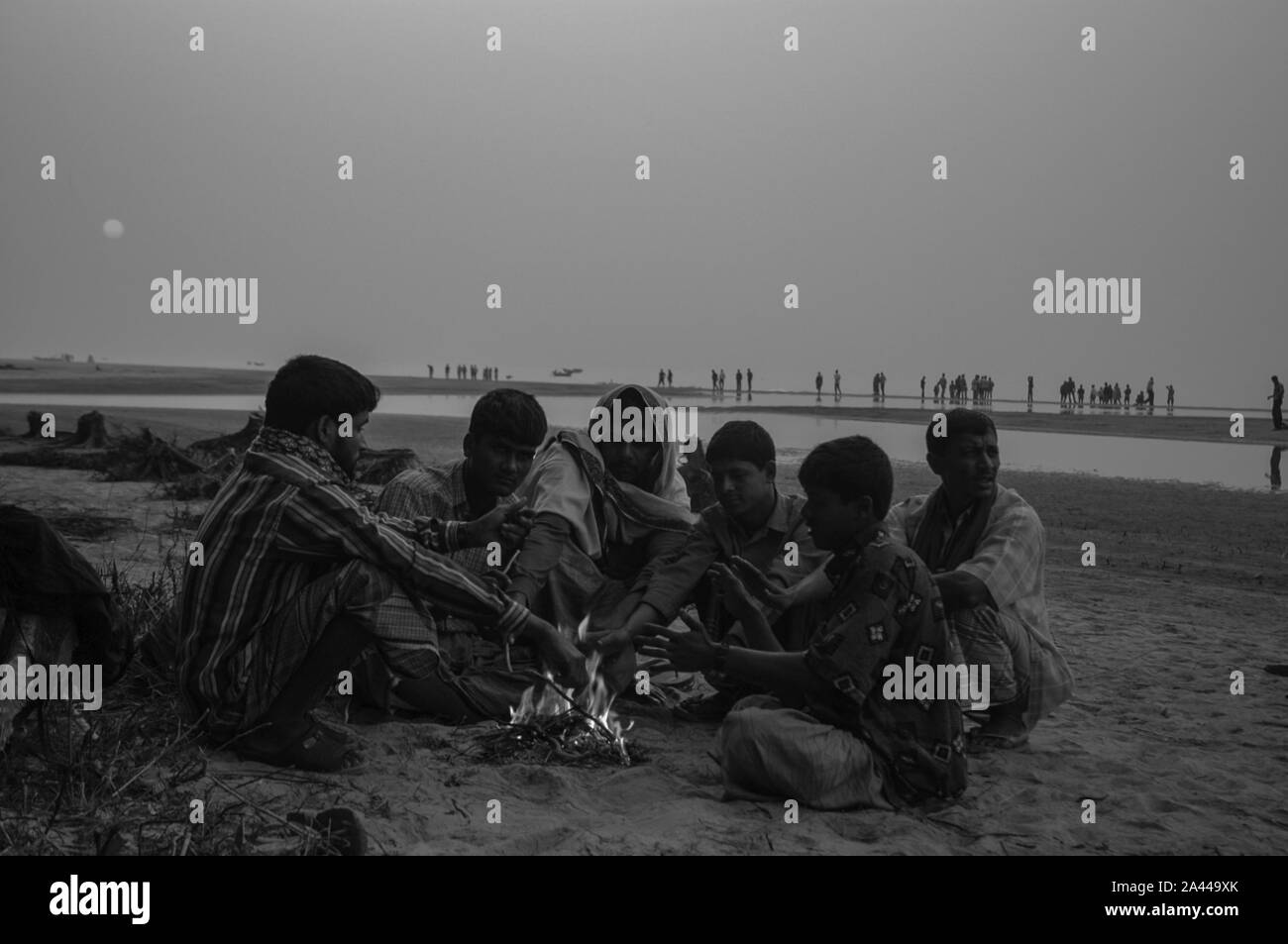 Persone a basso reddito stessi caldo nel calore dalla combustione di rifiuti in un inverno mattina Kuakata a mare spiaggia. Patuakhali, Bangladesh. Foto Stock