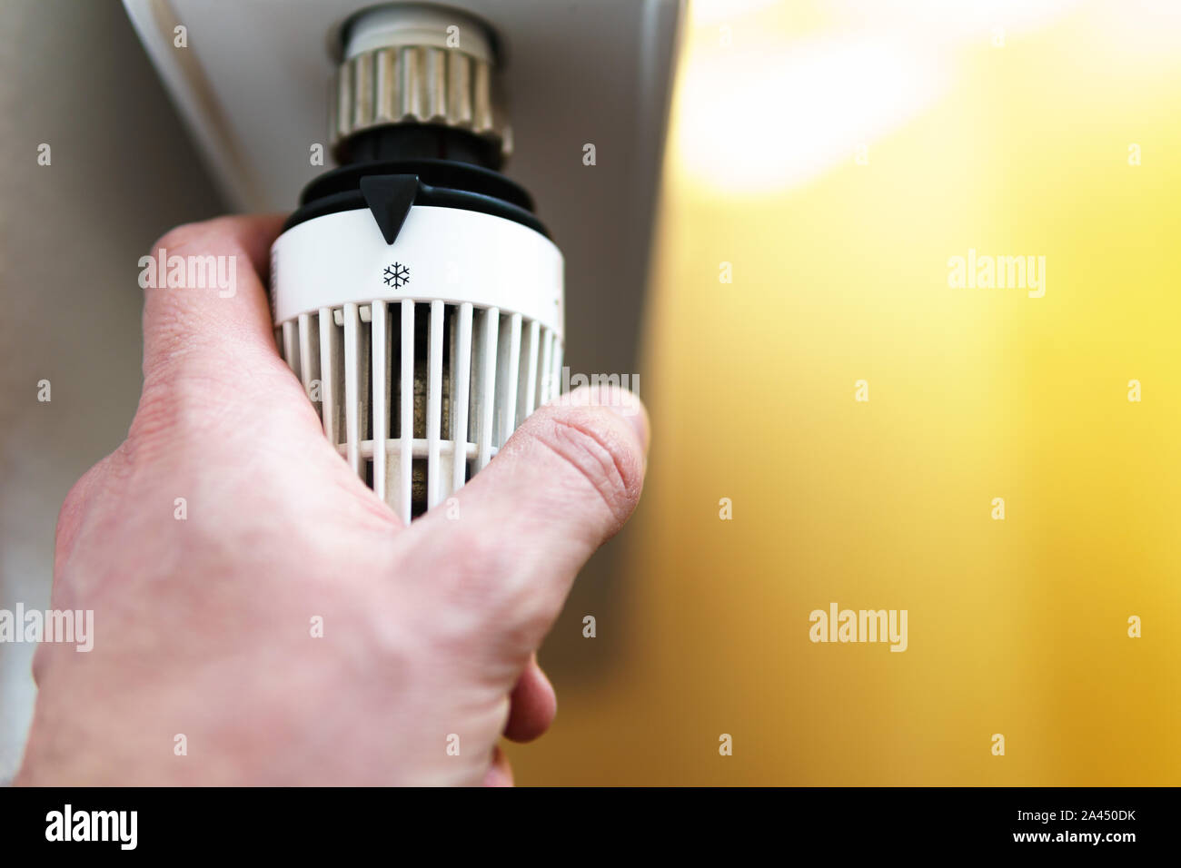 Mano di uomo regolazione valvola del termostato del radiatore a fiocco di neve icona di brina, simbolo per risparmiare soldi a spese di riscaldamento o a bassa temperatura, closeup, horizo Foto Stock