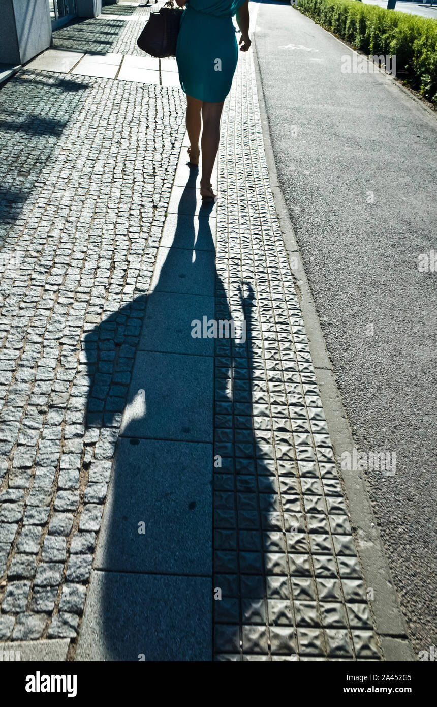 donna che cammina via, proiettando una lunga ombra Foto Stock