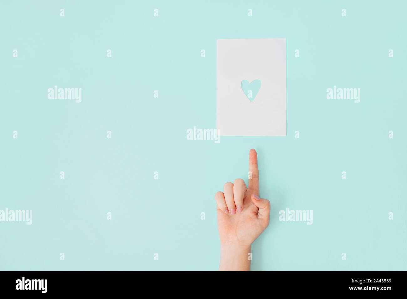 Femmina con mano manicure su un corallo bianchita di puntamento di sfondo a un foglio di carta bianco con cuore foro sagomato in esso. Foto Stock