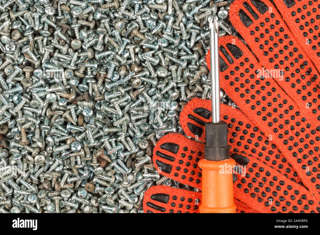 Guanti da lavoro e un cacciavite giacente su un mucchio di viti. Vista superiore Foto Stock