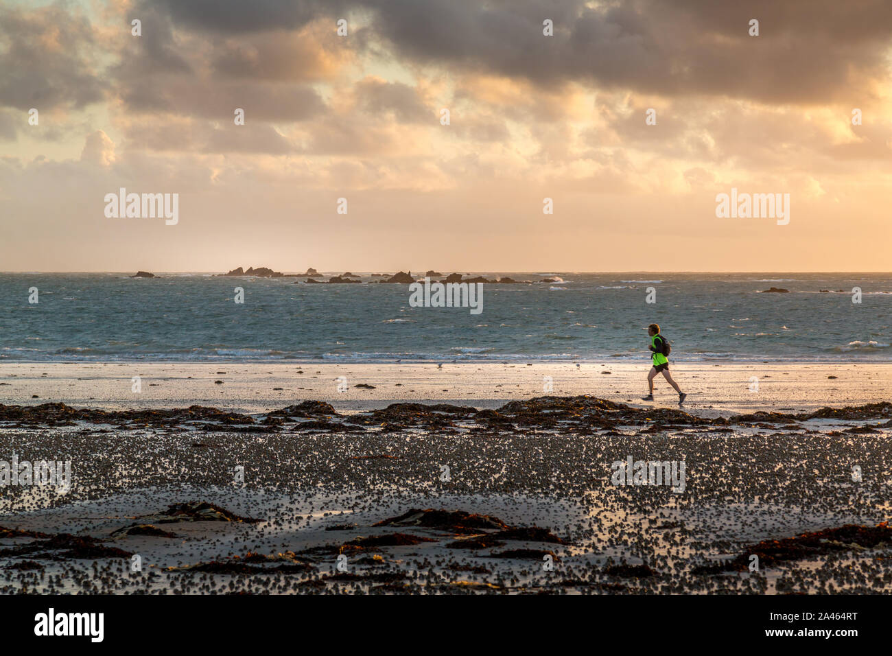 Una persona jogging o in esecuzione su una spiaggia in jersey sulle Isole del Canale, al tramonto. Foto Stock