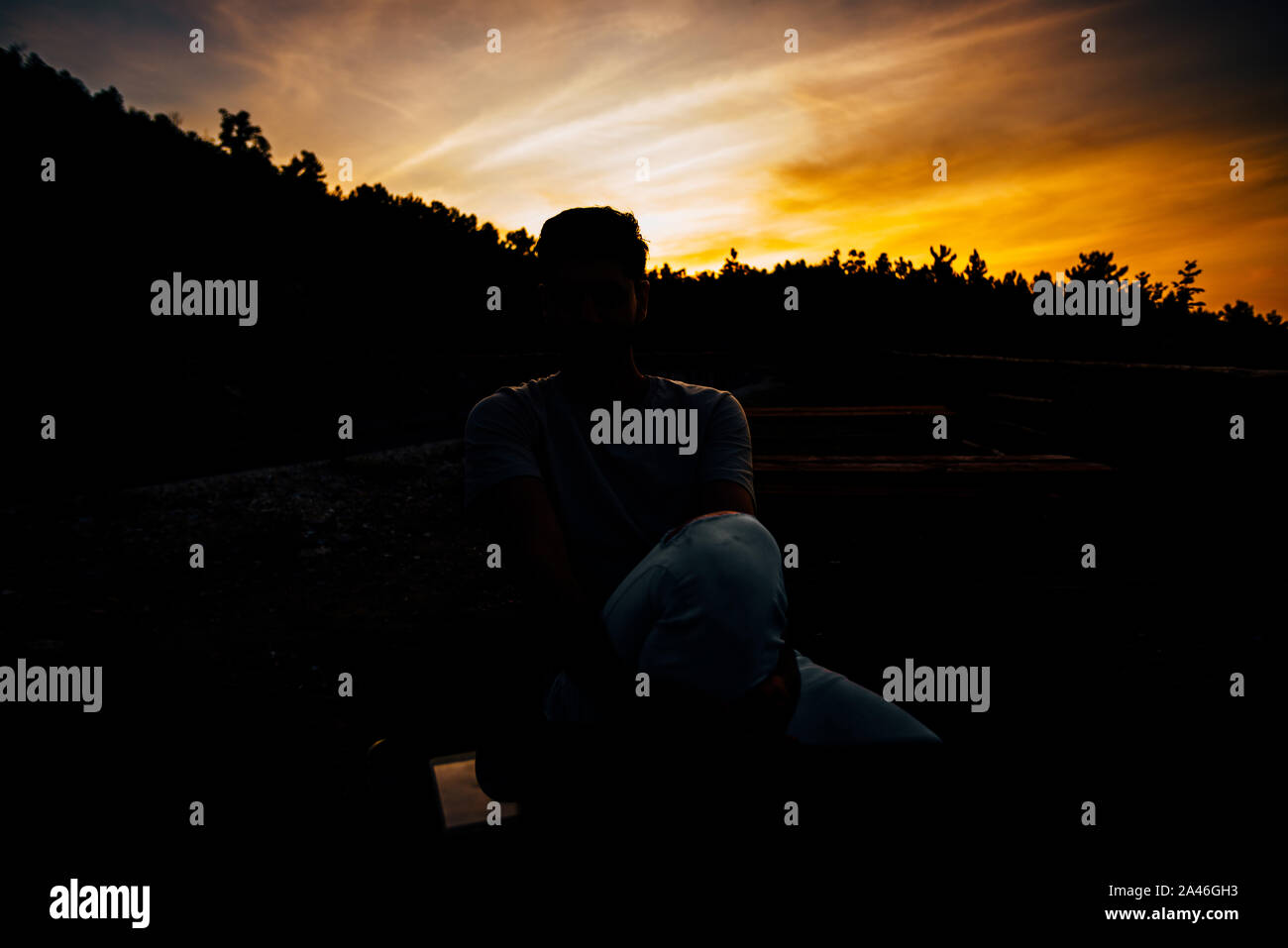 Rilassata americano africano giovane uomo seduto e in attesa sulla panchina contro il cielo al tramonto Foto Stock