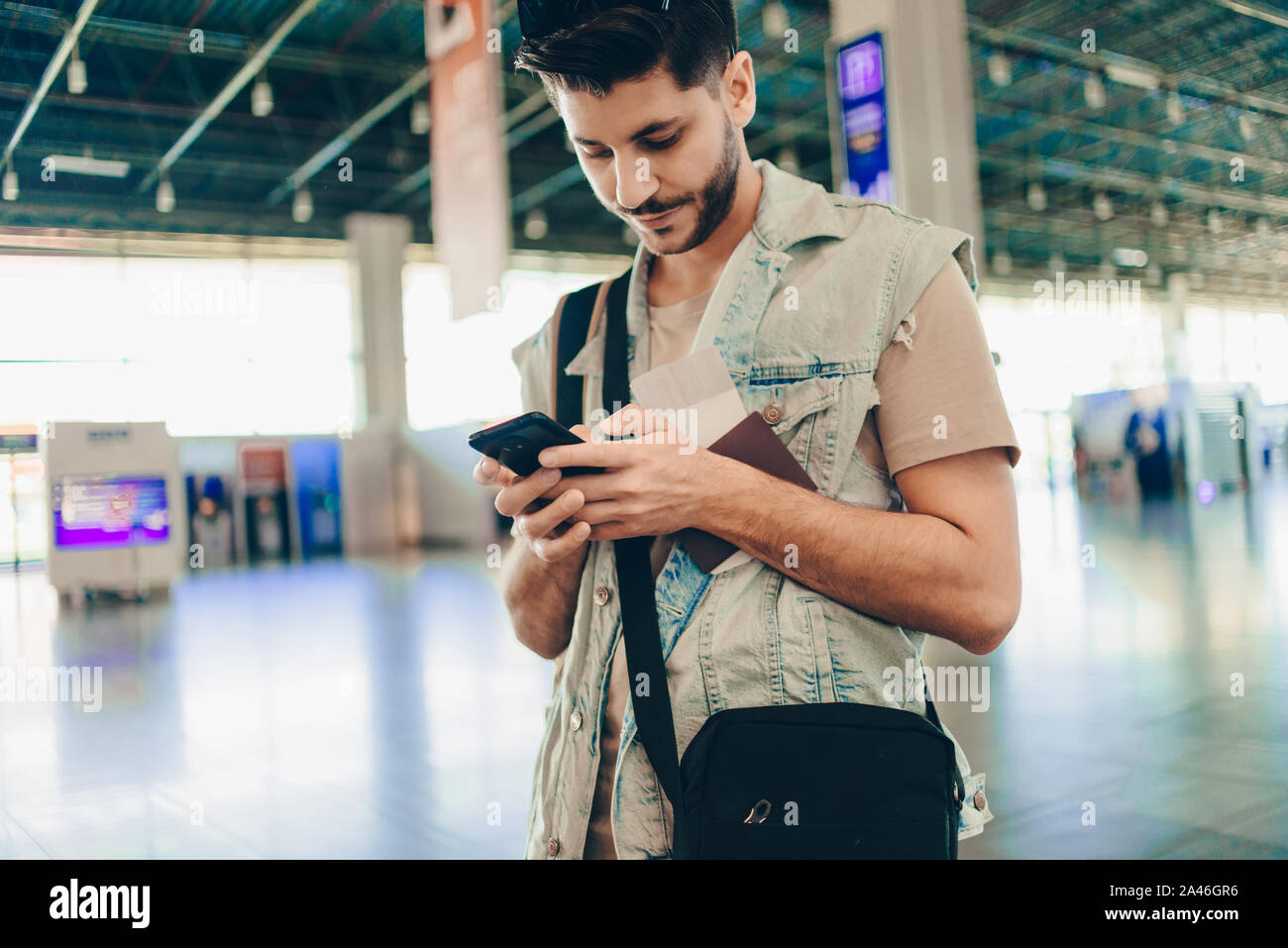 Giovane viaggiatore con passaporto e i biglietti utilizzando il telefono cellulare all'aeroporto Foto Stock