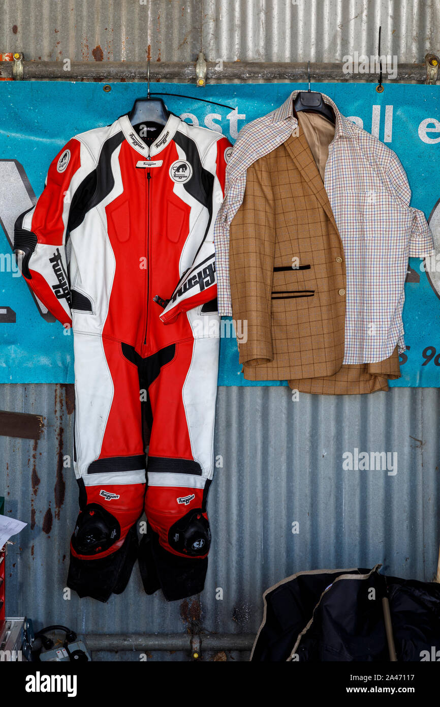 Motociclo paddock garage con Furygan pelli di equitazione e giacca sportiva appeso alla parete posteriore al 2019 Goodwood, Sussex, Regno Unito. Foto Stock