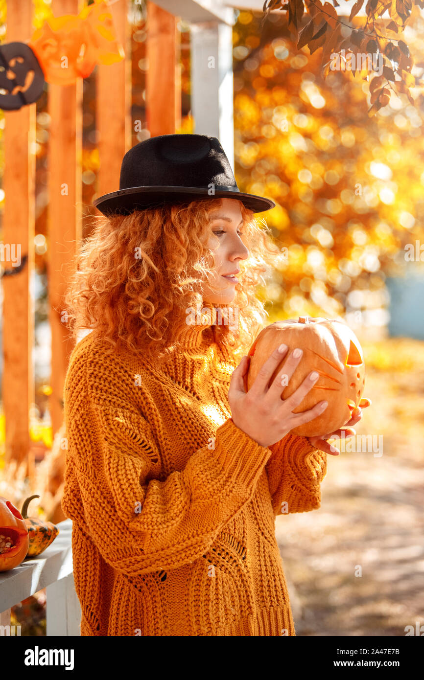 Halloween Preparaton concetto. Giovane donna in hat in piedi all'aperto con jack-o-lantern pensieroso Foto Stock