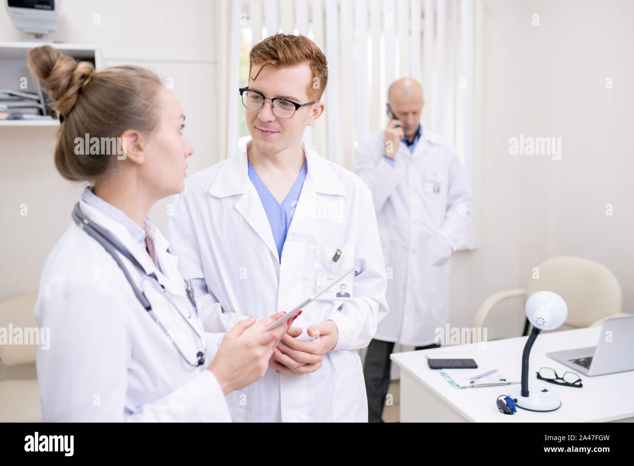 Due giovani colleghi in whitecoats discutendo di materiale medico in cliniche Foto Stock