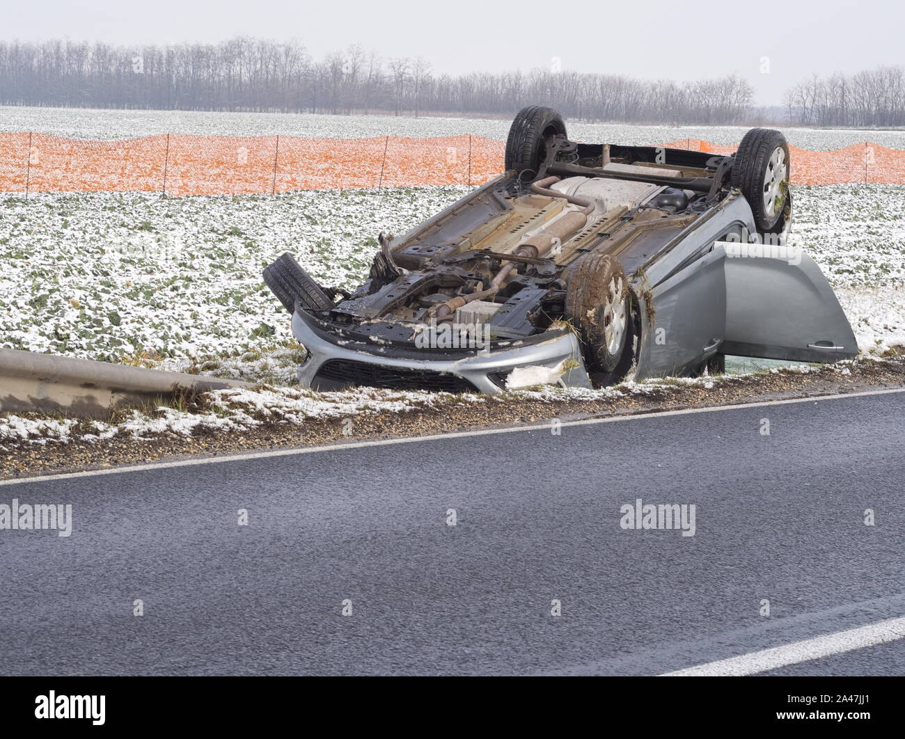 Auto ribaltata accanto alla strada bagnata in una giornata invernale Foto Stock