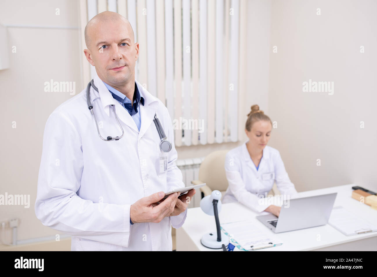 Bald seri professionisti in camice bianco guardando attraverso i dati online in cliniche Foto Stock