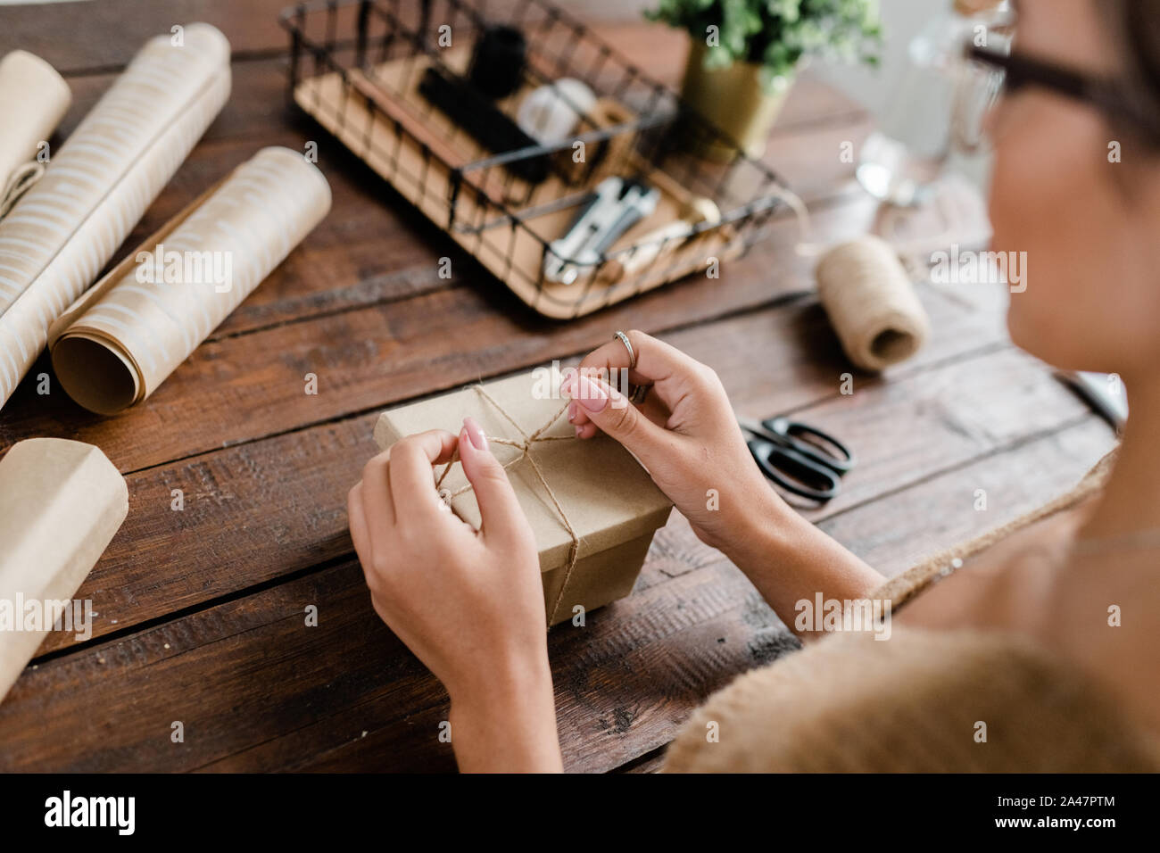 Le mani del giovane femmina rendendo il nodo sulla sommità del giftbox mentre doni di imballaggio Foto Stock