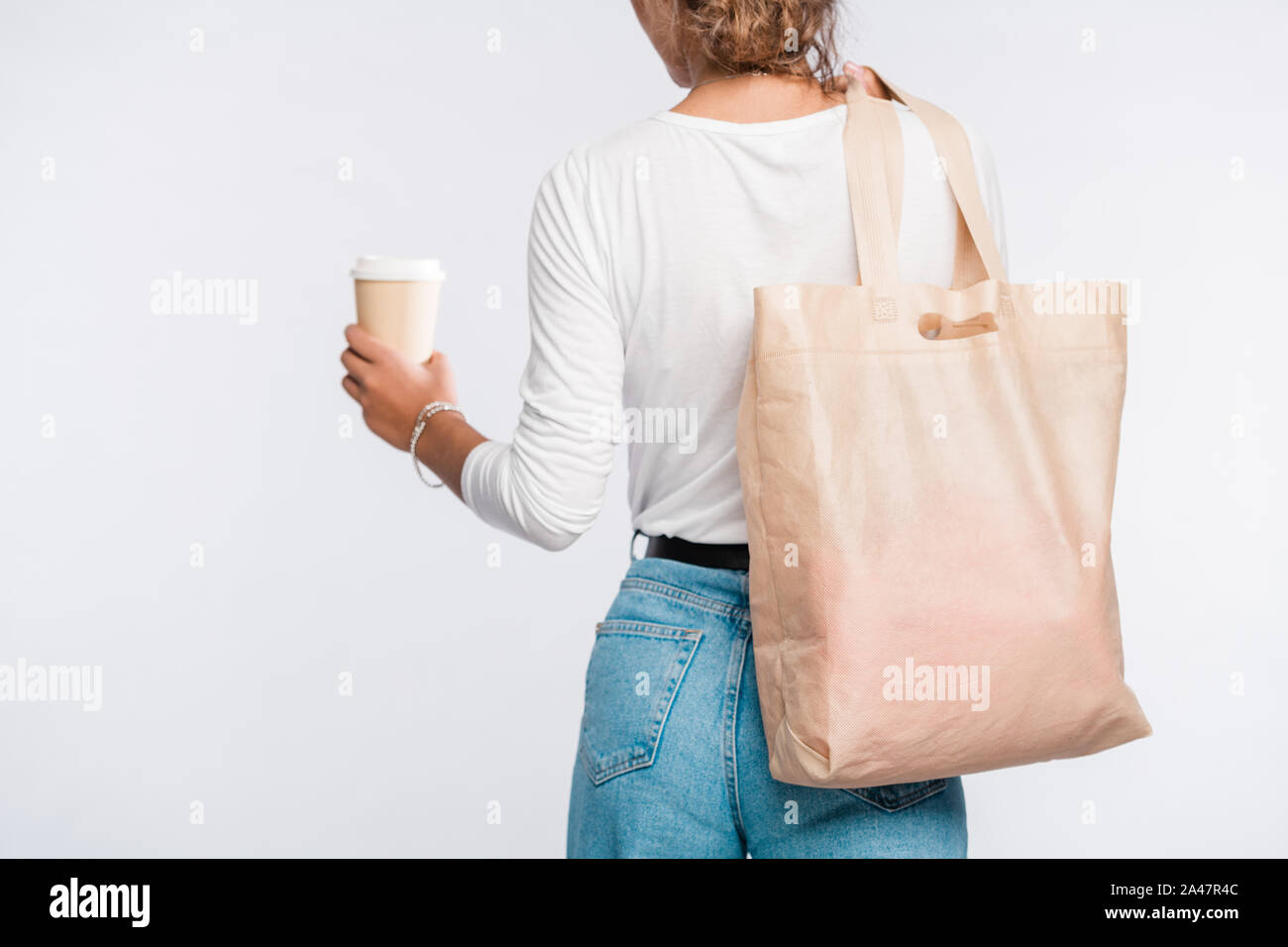 Vista posteriore della giovane donna in informale che porta bicchiere di caffè e borsetta Foto Stock