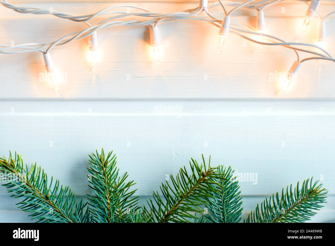 L'abete bianco e giallo caldo le luci di Natale in bianco sullo sfondo di legno. Anno nuovo concetto. Copia gratuita dello spazio. Foto Stock