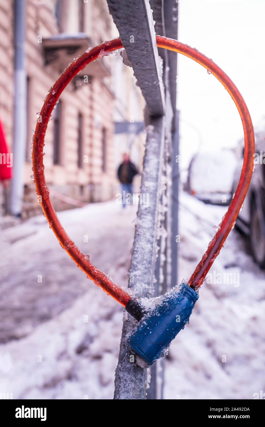 Bike blocco cavo appeso sul recinto durante il gelo, ricoperta di ghiaccio, vicino alla strada accanto alle automobili per impedire il furto, il ladro o il passer è offuscata nel Foto Stock