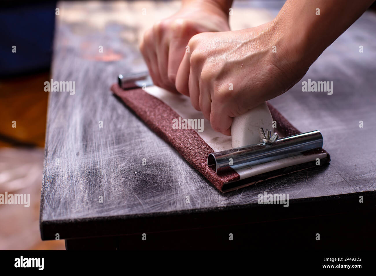 Persona prepara la superficie per la verniciatura e levigatura dalle mani di un vecchio legno nero tabella con un manuale di falegnameria titolare sandpapers Foto Stock