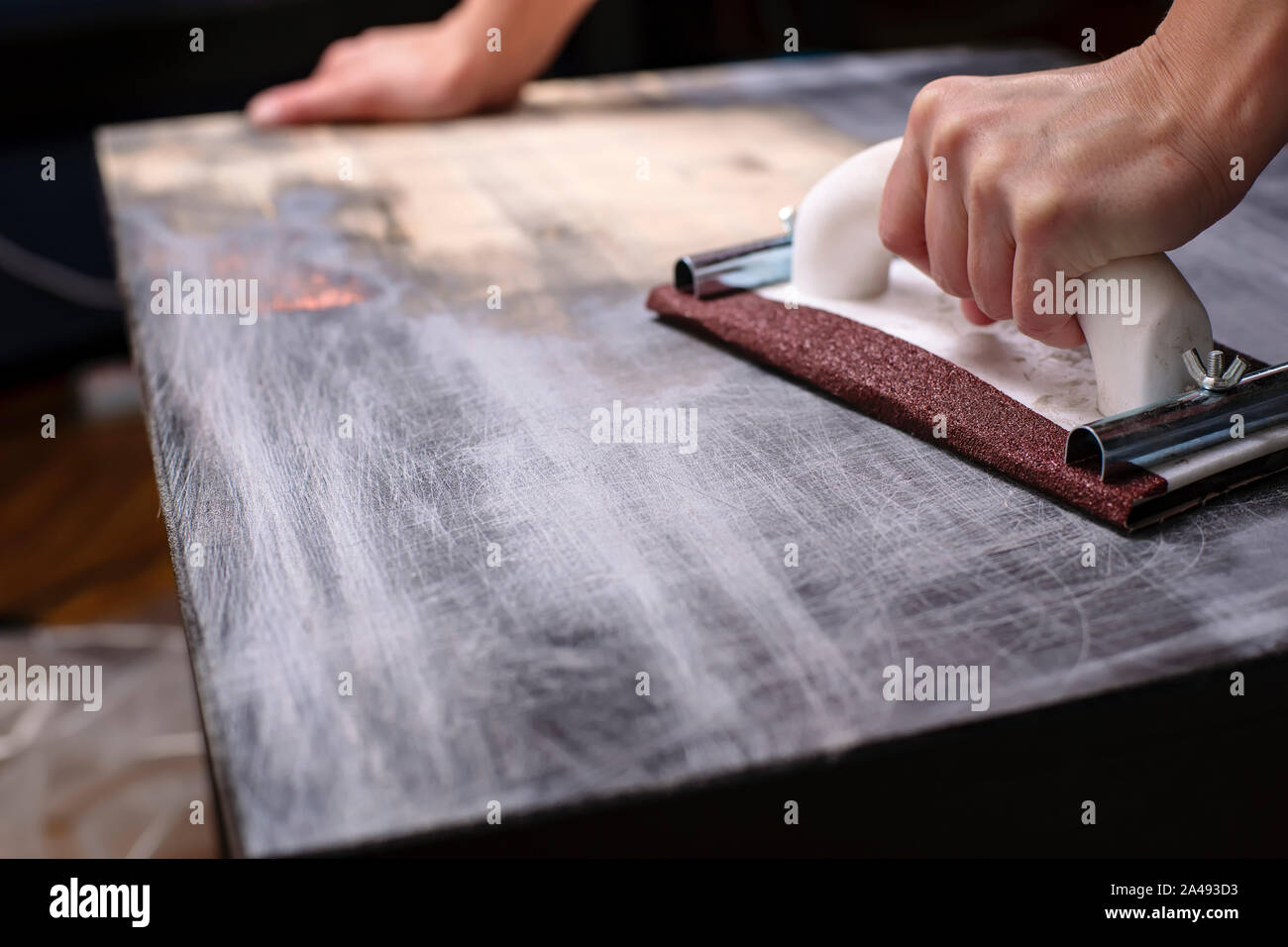 Persona prepara la superficie per la verniciatura e levigatura dalle mani di un vecchio legno nero tabella con un manuale di falegnameria titolare sandpapers Foto Stock