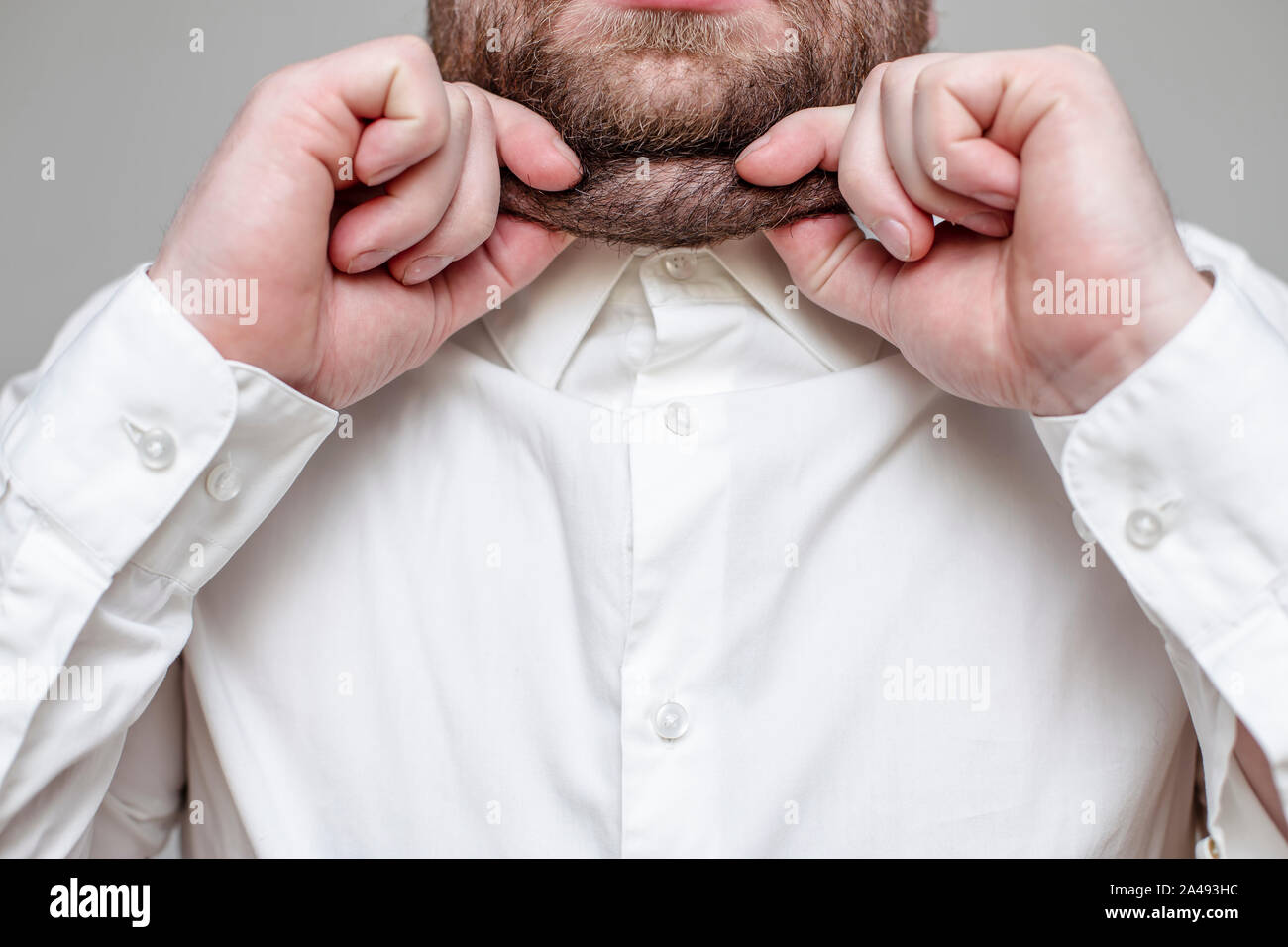 Persona barbuto pizzicare su se stesso il suo doppio mento, indossa una camicia bianca su sfondo grigio Foto Stock