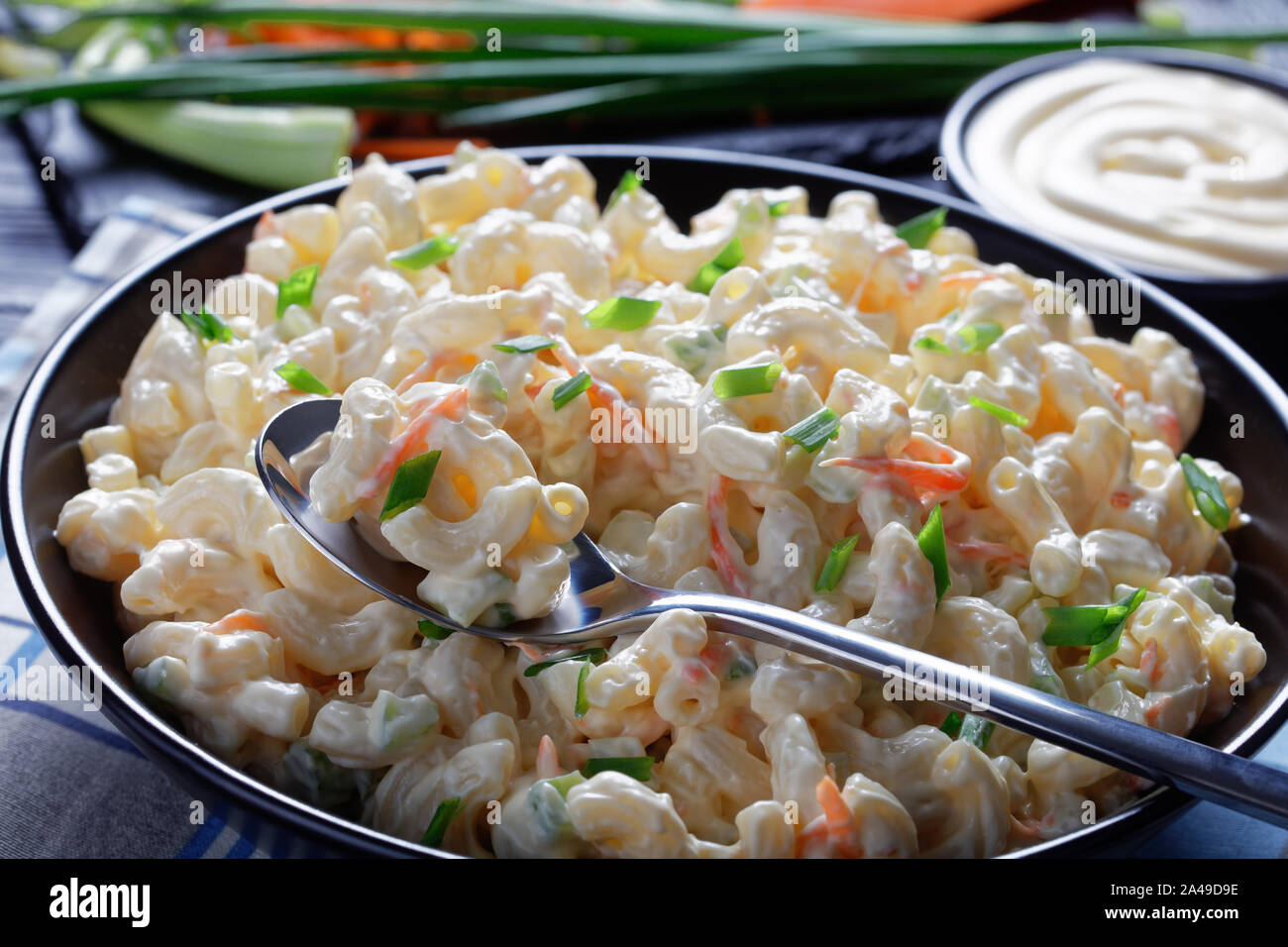 Close-up di american maccheroni con Insalata di carote grattugiate, sedano, cipolline e maionese la salsa in un recipiente di nero su un tavolo di legno, orizzontale Foto Stock