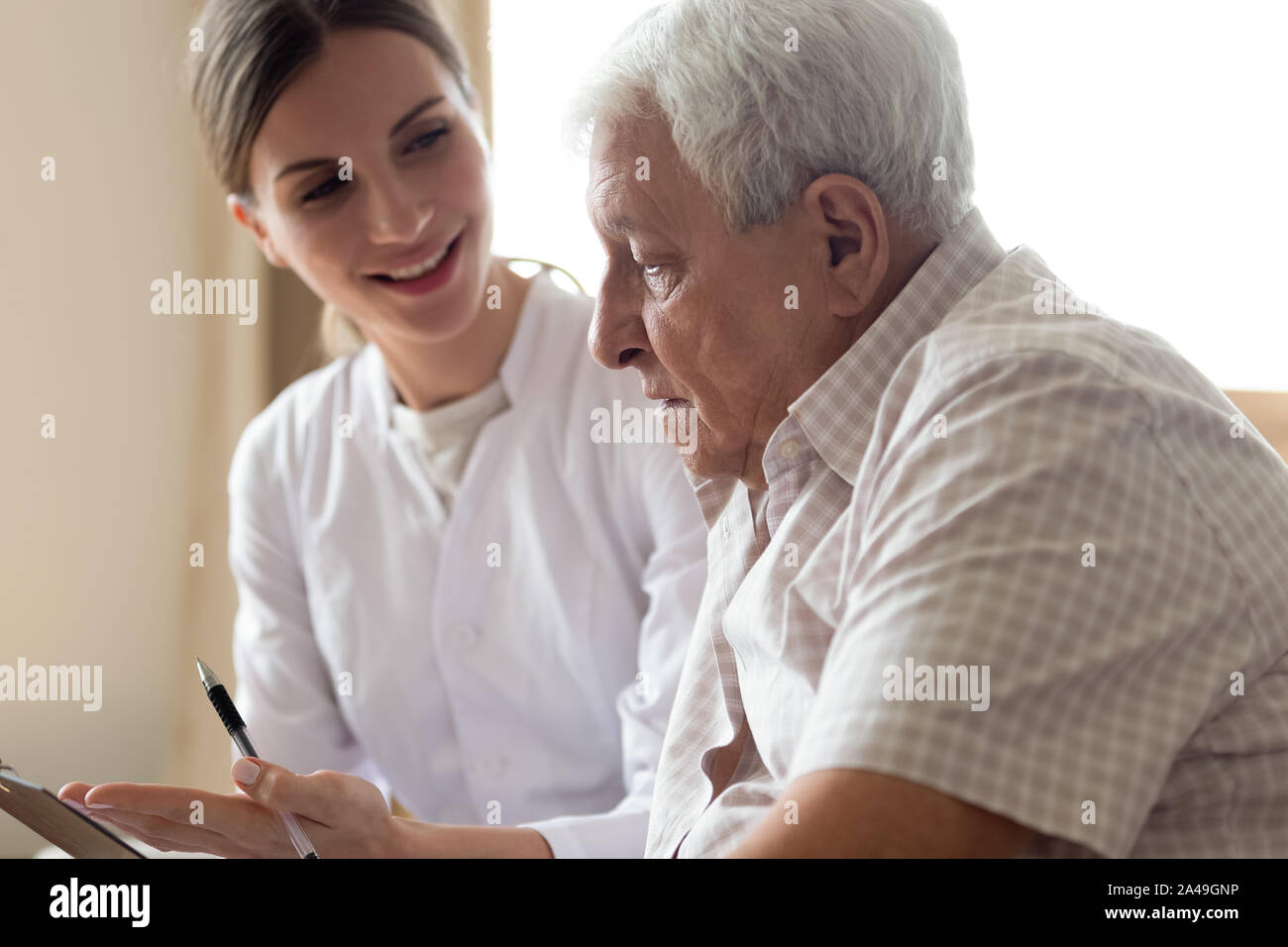 Uomo vecchio paziente e giovane infermiere parlando in ambienti interni Foto Stock