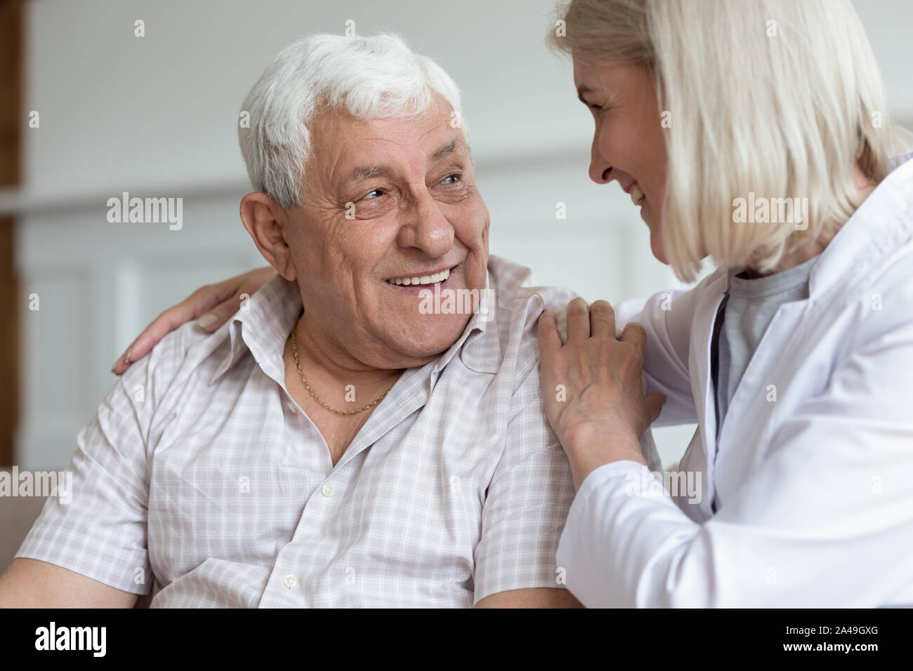 Di mezza età infermiera abbraccio uomo anziano seduta del paziente sul lettino Foto Stock
