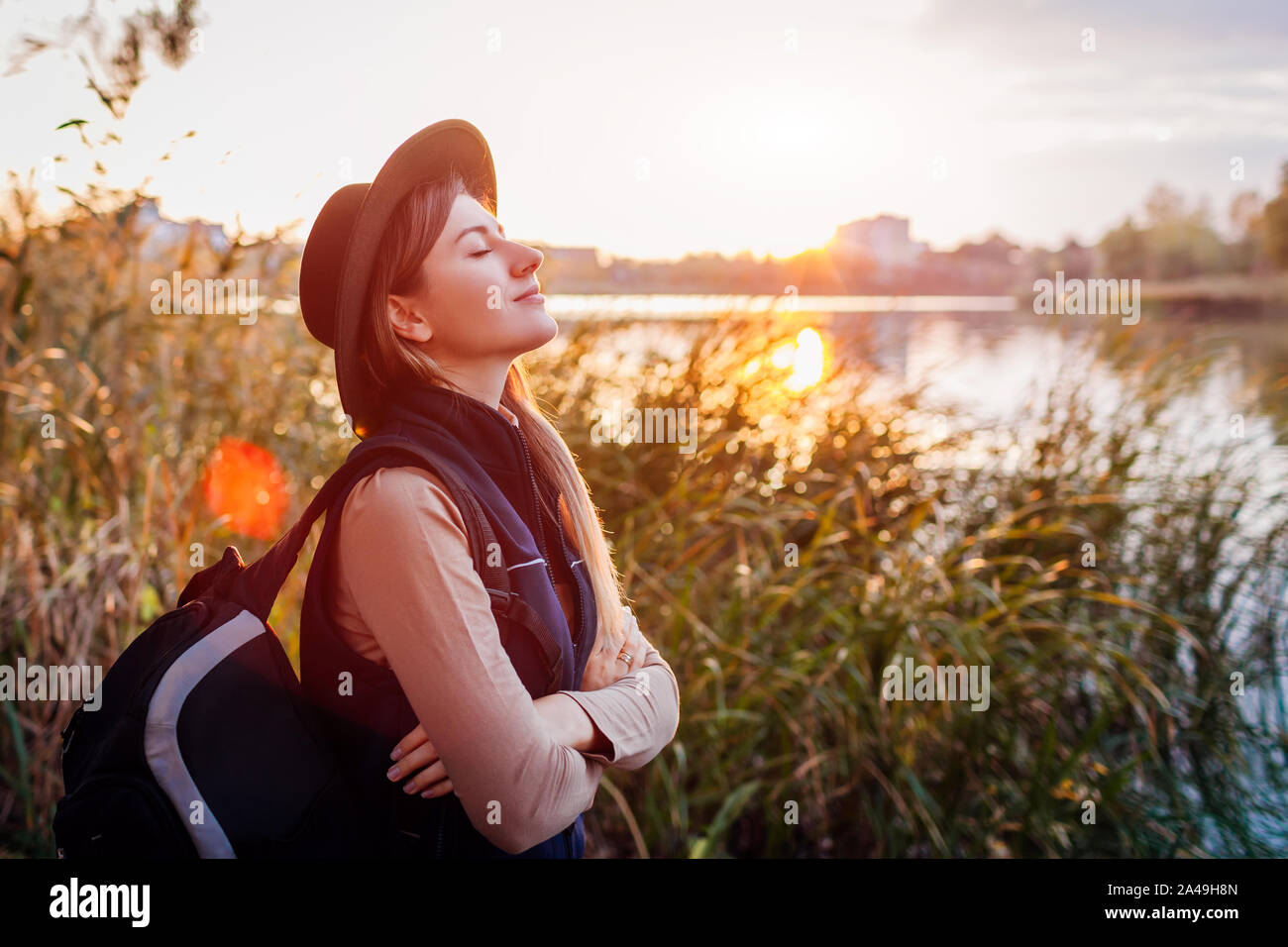 Viaggiatore con zaino rilassante da autunno river al tramonto. Giovane donna respirazione profonda sensazione felice e libera Foto Stock