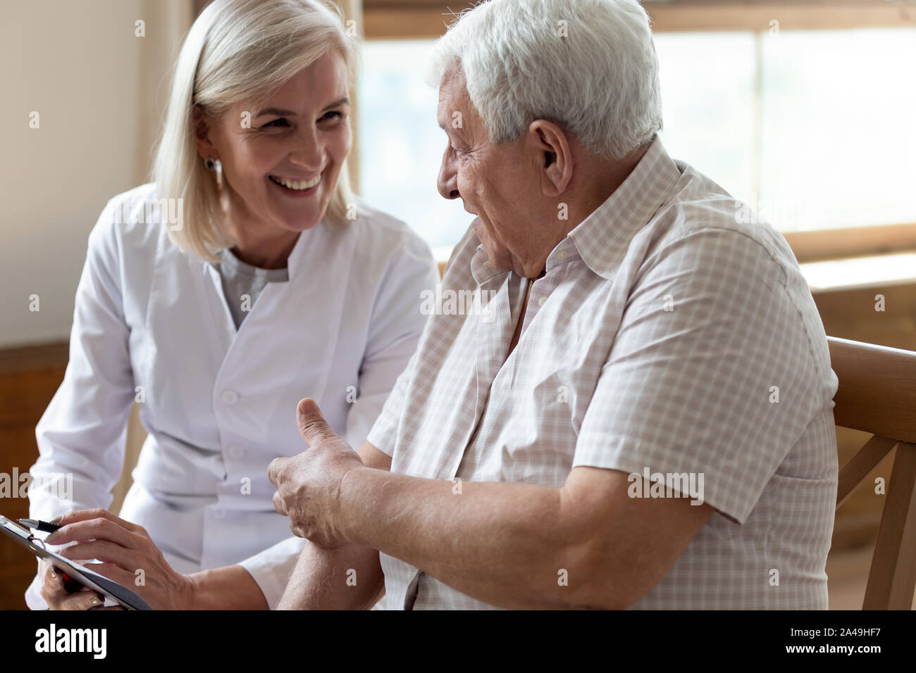 Uomo anziano paziente e di mezza età infermiera parlando in ambienti interni Foto Stock