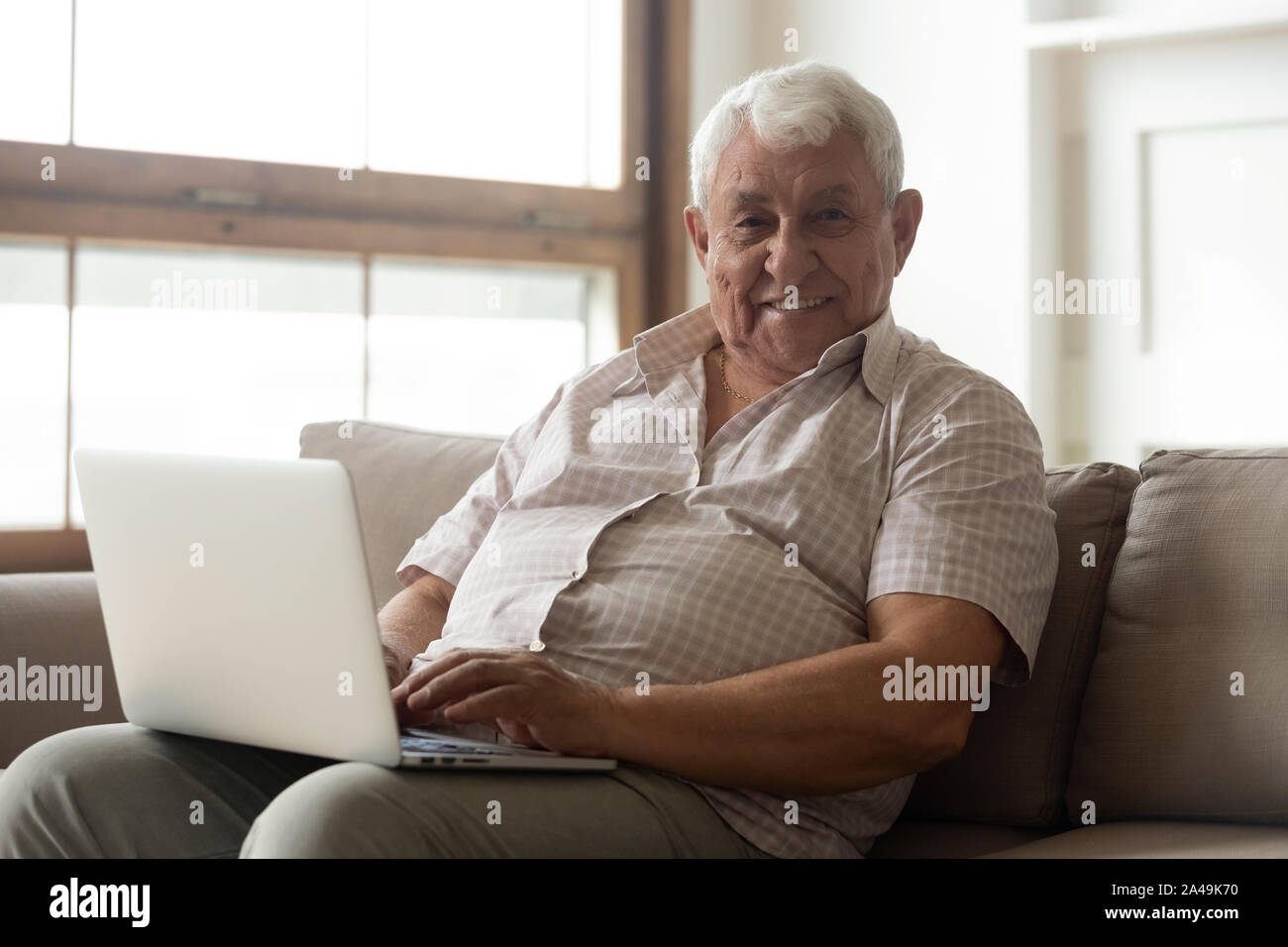 80s uomo seduto sul divano con il computer portatile guardando la fotocamera Foto Stock
