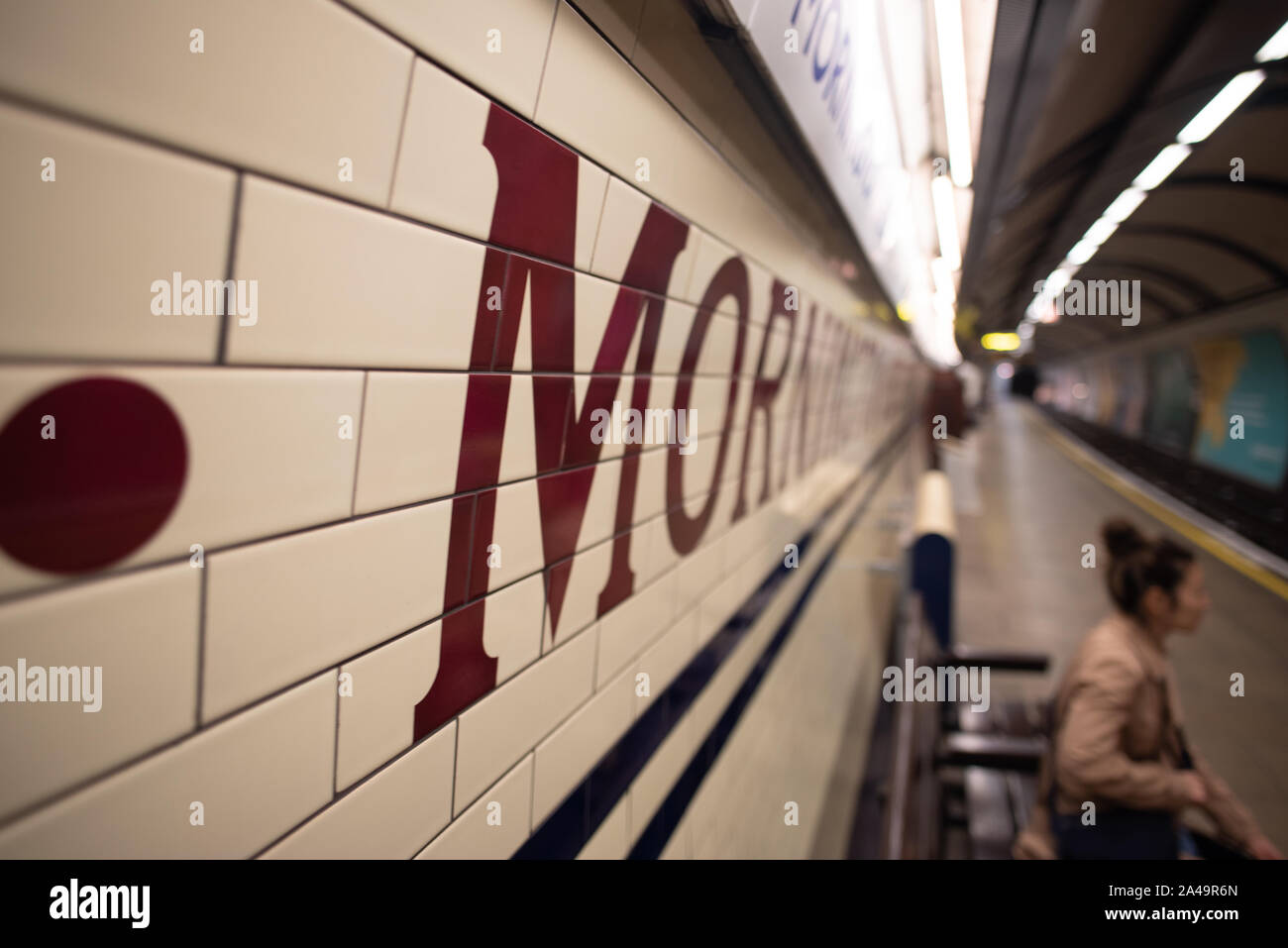 London, Regno Unito - 15 Settembre 2019: una donna attende il tubo sotto le piastrelle ecru e segno di Mornington Crescent, una stazione della metropolitana. Foto Stock