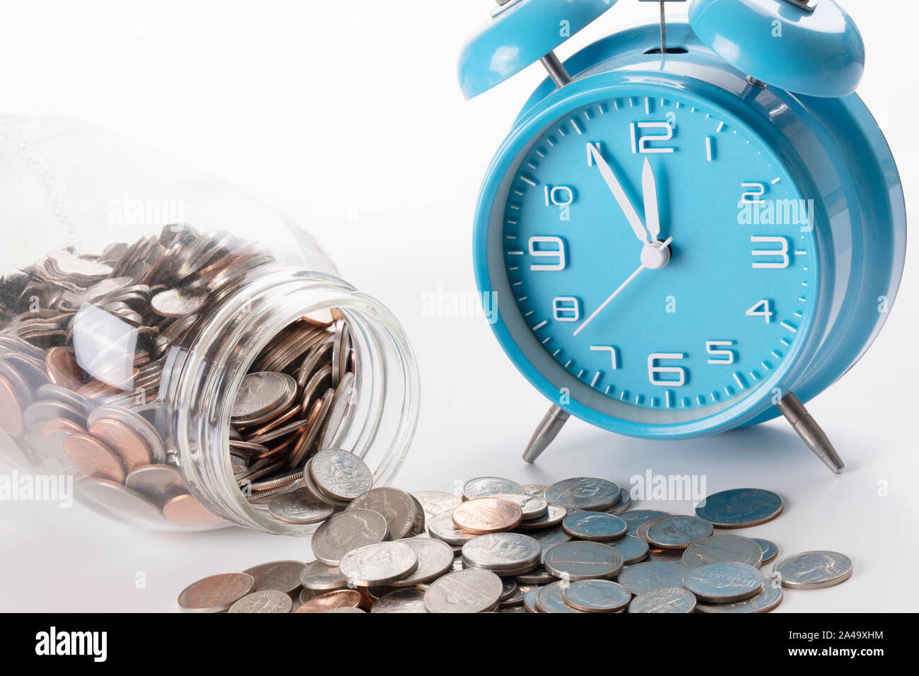 Noi di monete in un vaso isolato su sfondo bianco con un orologio sveglia con spazio di copia Foto Stock