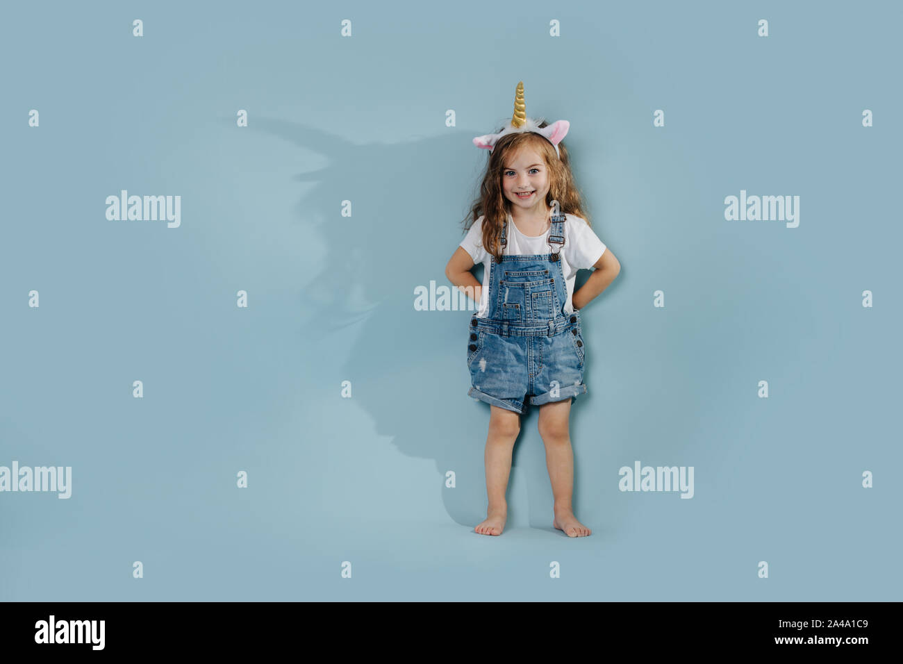 Toddler sorridente ragazza che indossa la fascia di unicorn su sfondo blu Foto Stock