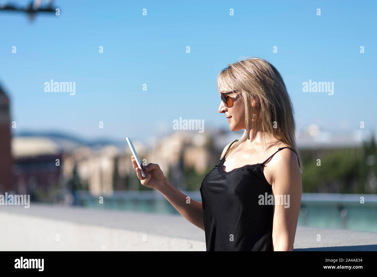 Vista laterale di una ragazza bionda controllando uno smart phone su strada Foto Stock