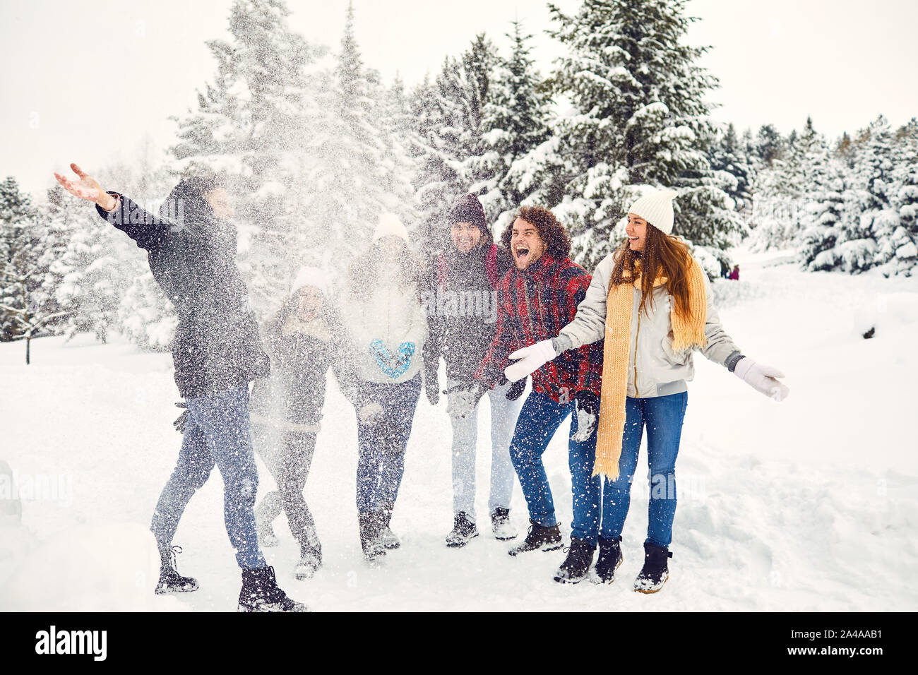 Gruppo di entusiasti persone gettando cumulo di neve bianca e ridere in polvere di cristallo in piedi vicino nei boschi Foto Stock