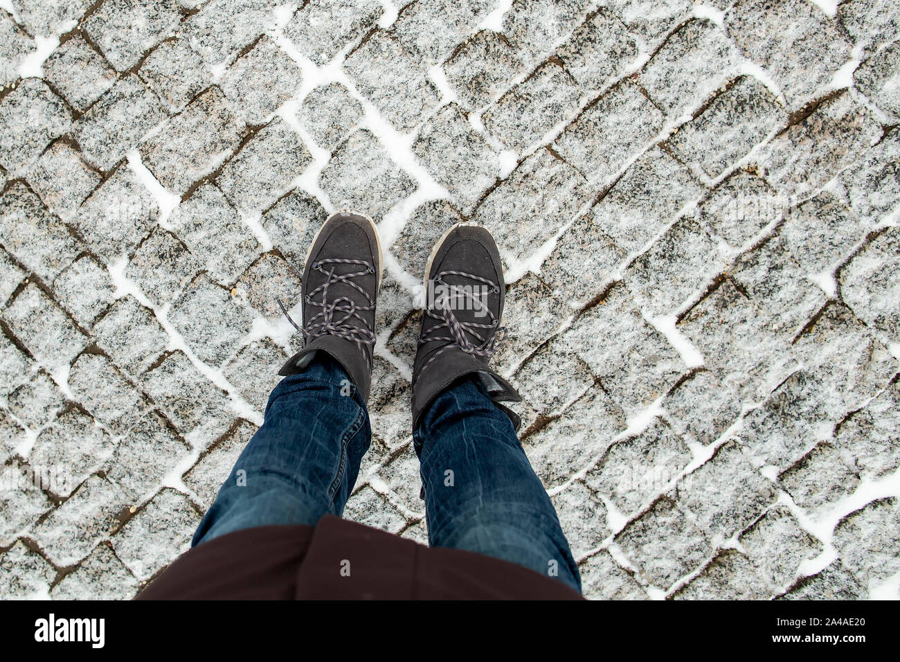 Le donne per le gambe in eleganti stivali in pelle scamosciata stand sulla neve-coperta di pavimento di granito acciottolato, su un inverno freddo giorno. Foto Stock