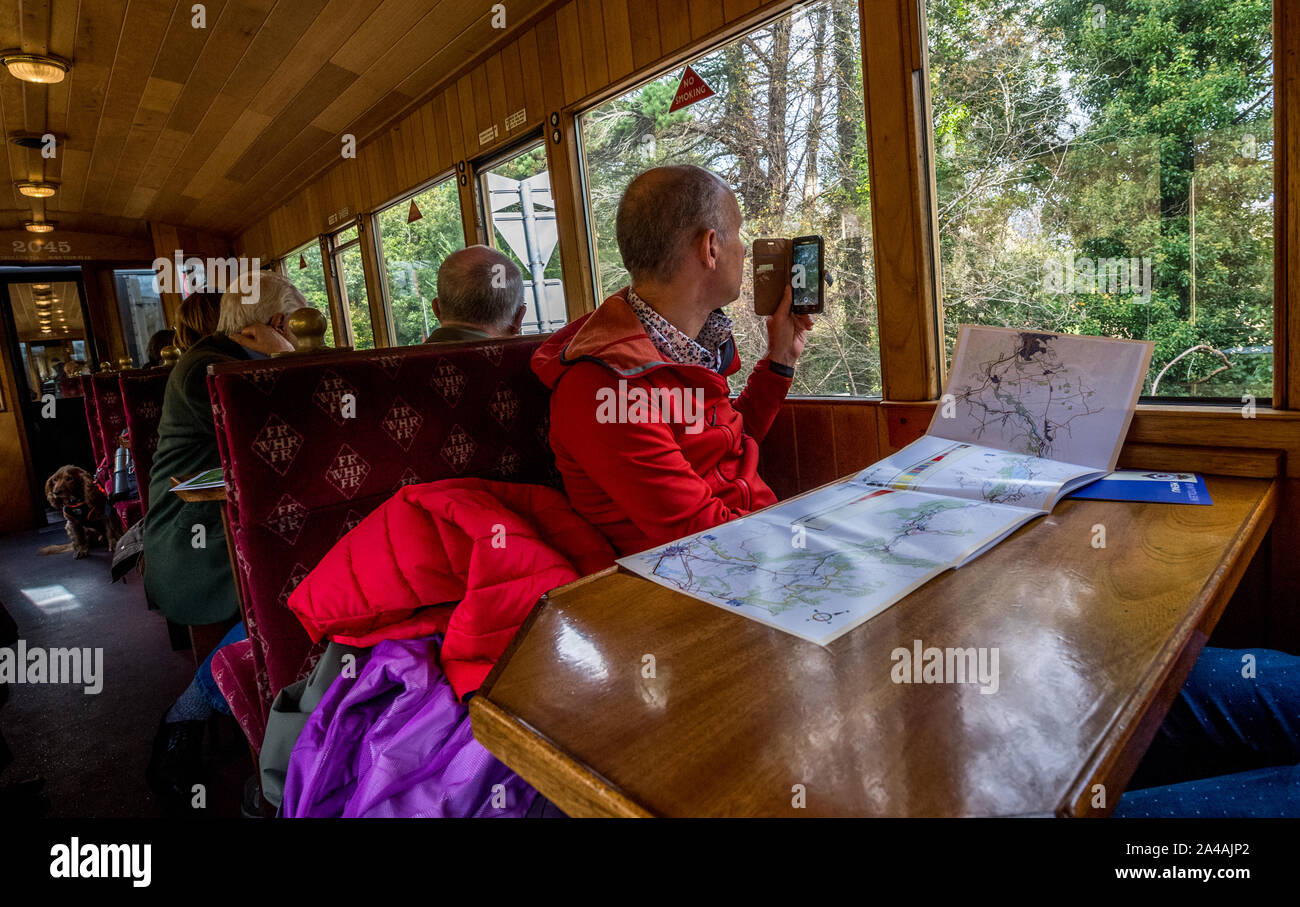 Fotografare passeggeri utilizzando un telefono cellulare all'interno di una rampa coach sul Ffestiniog & Welsh Highland Railway con una mappa del percorso del treno sul tavolo Foto Stock