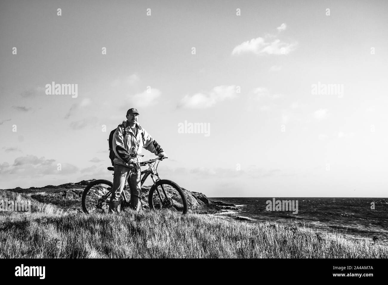Escursioni in bicicletta in Irlanda. Ciclista ricreative con mountain bike e zainetto sul bordo delle dune di sabbia guardando il mare. In bianco e nero. Foto Stock